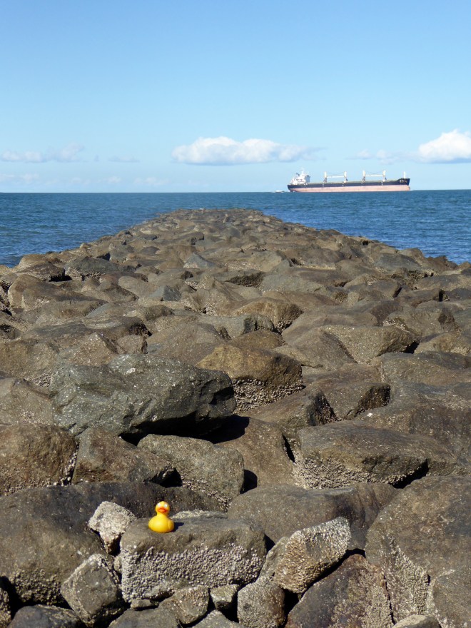 Rocks at end of pier and ship on Maputo Bay